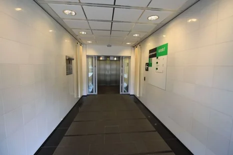 Hal met witte muren en een donkere vloer die leidt naar een lift in het gebouw aan het Herculesplein.