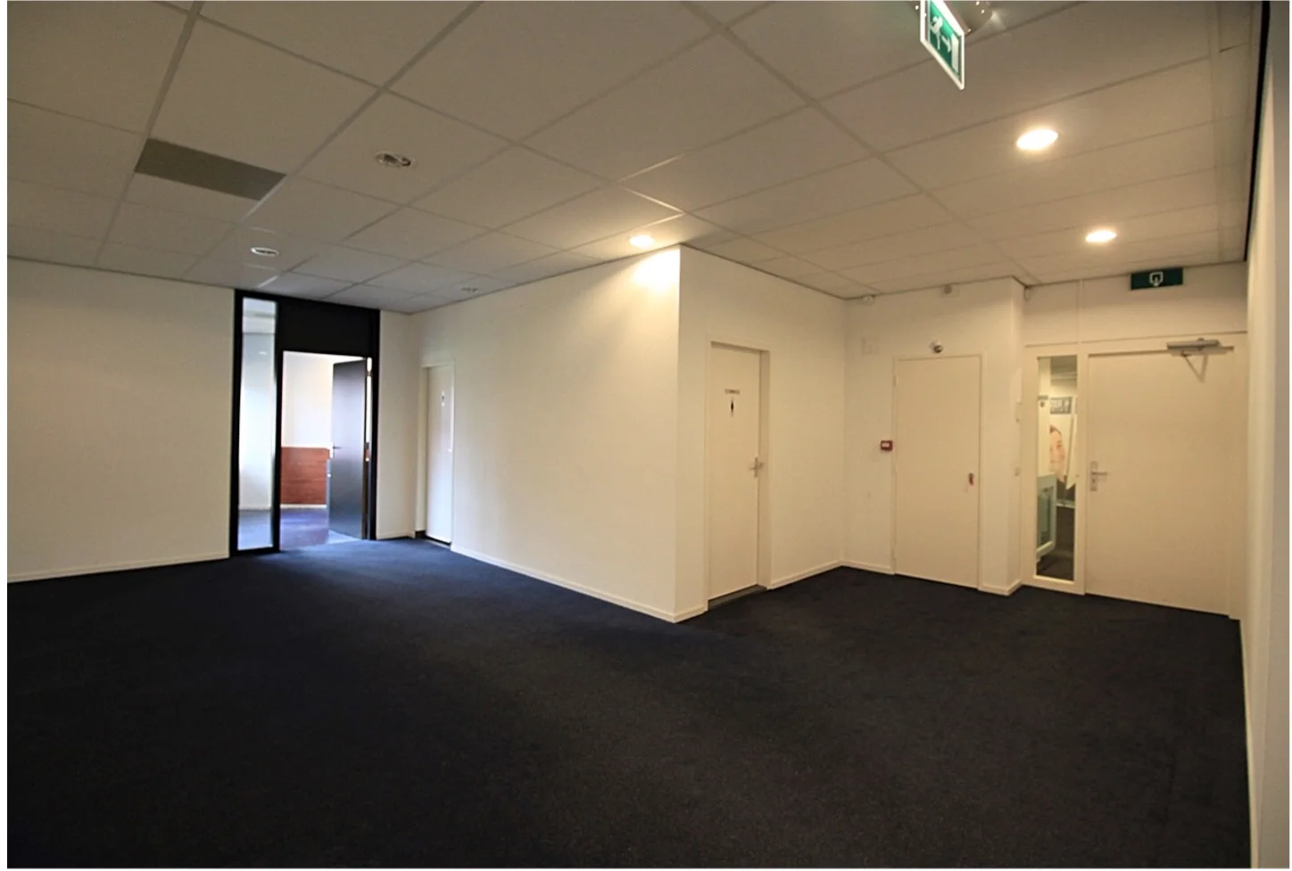 Leeg kantoorpand met blauwe vloerbedekking op het Herculesplein, met meerdere gesloten deuren en een open deur naar een aangrenzende ruimte.