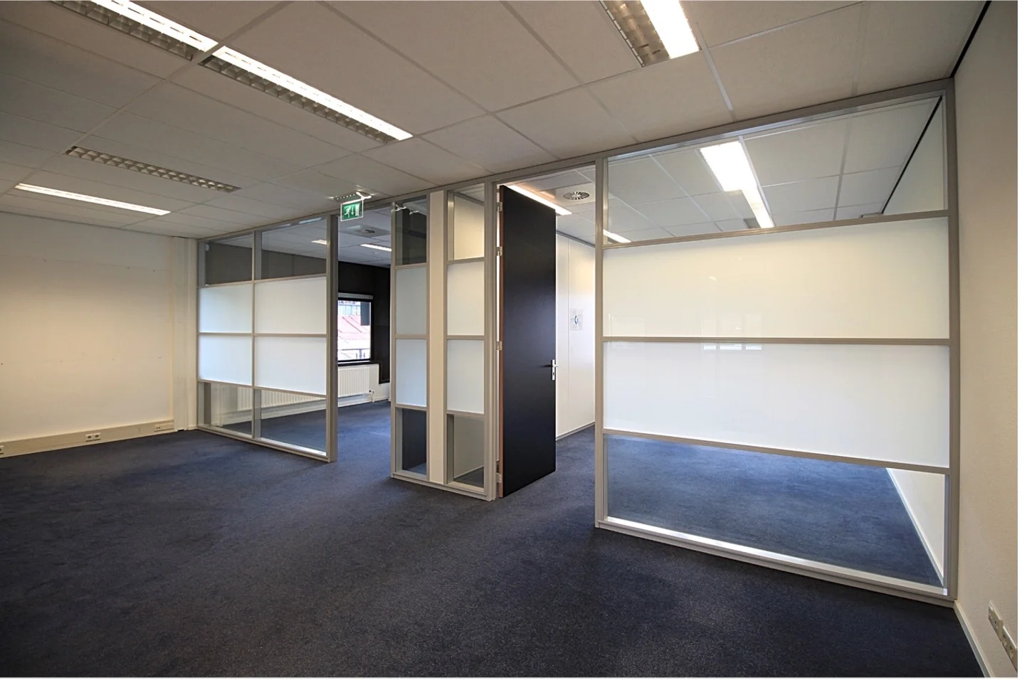 Licht en modern kantoorpand aan het Herculesplein met glazen scheidingswanden en donkerblauwe vloerbedekking.