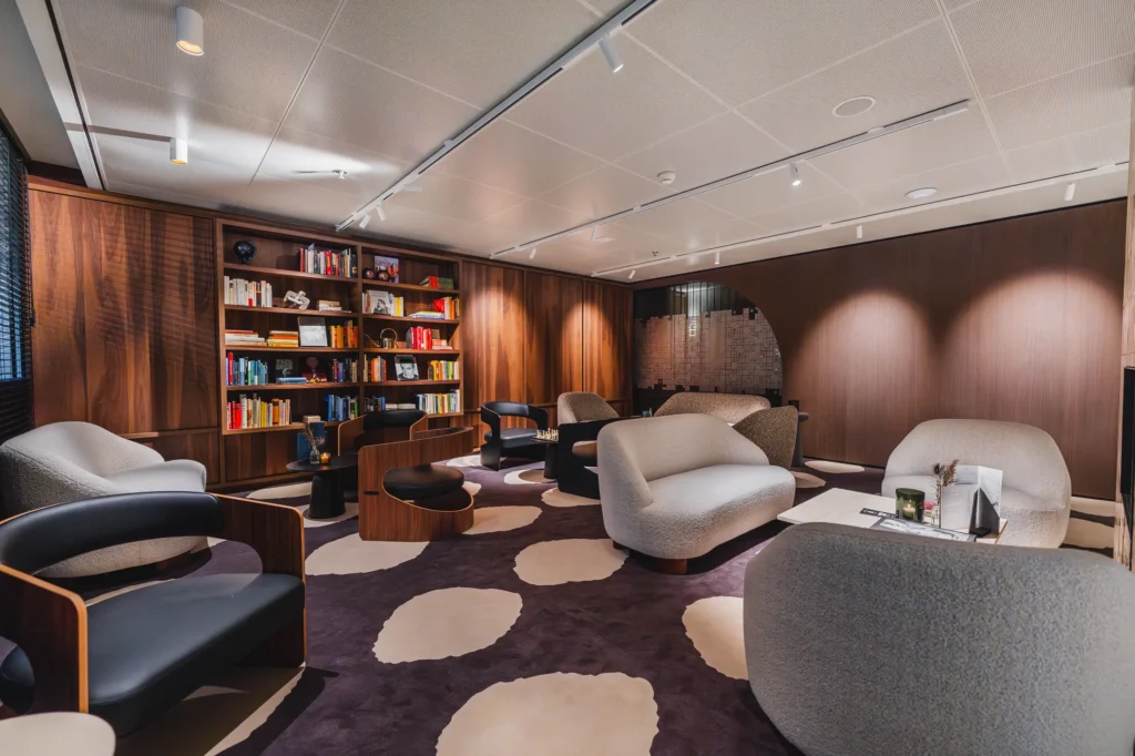 Een moderne, gezellige zithoek met comfortabele banken, stoelen en een gevulde boekenkast.