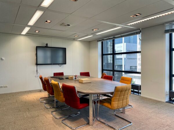 Vergaderkamer aan het Weena met kleurrijke stoelen rond een grote tafel, een scherm aan de muur en uitzicht op moderne kantoorpanden.