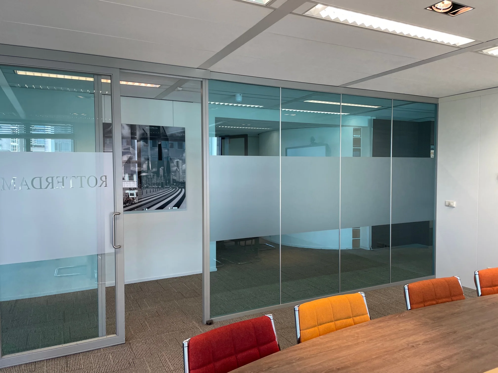 Vergaderruimte met glazen wanden en gekleurde stoelen aan een houten tafel in kantoorgebouw aan het Weena in Rotterdam.