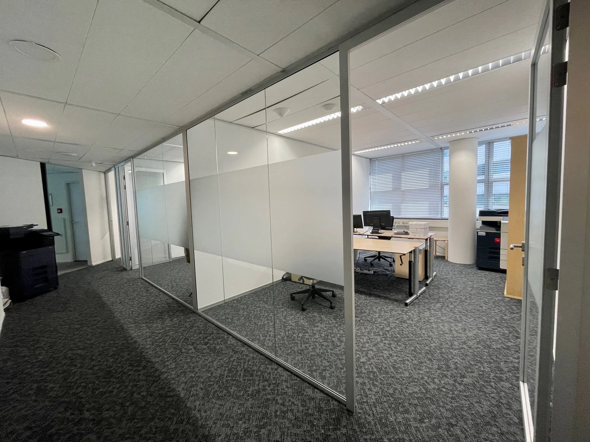 Moderne kantoorruimte aan de Weena met glazen wanden, bureaus, computers en een printer.