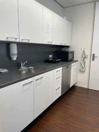 Moderne kantoorkeuken met witte kastjes, een spoelbak, magnetron en vaatwasser aan het Weena.
