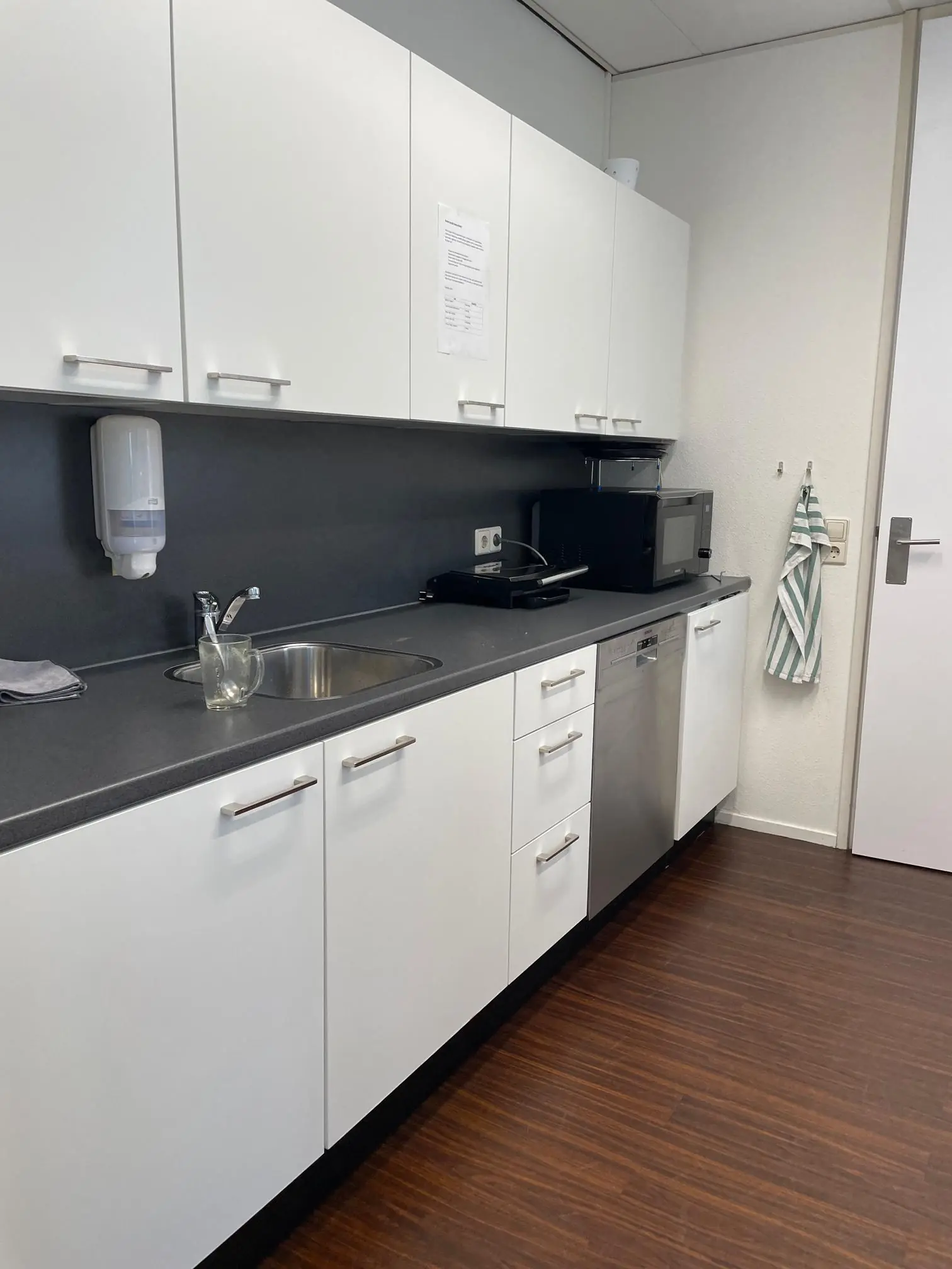 Moderne kantoorkeuken met witte kastjes, een spoelbak, magnetron en vaatwasser aan het Weena.