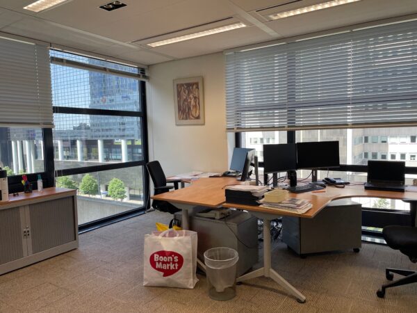 Kantoorruimte met meerdere bureaus, computers en een Boon’s Markt tas op de vloer, met uitzicht op het Weenagebouw in Rotterdam.