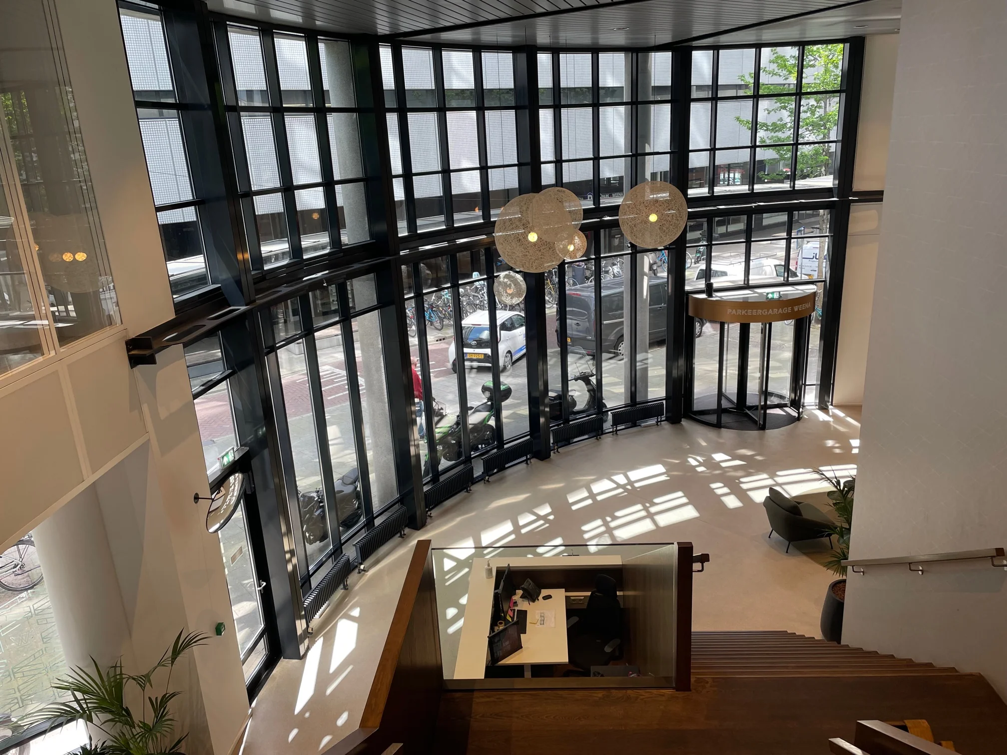 Ingangshal met grote glazen gevel en draaideur naar Parkeergarage Weena, gezien vanaf een houten trap binnenin het gebouw.