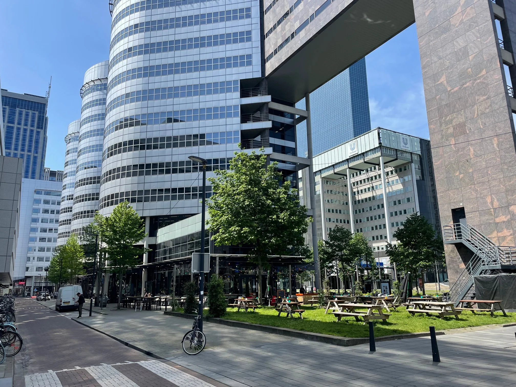 Moderne kantoorgebouwen en een groen plein met picknicktafels aan het Weena in Rotterdam.