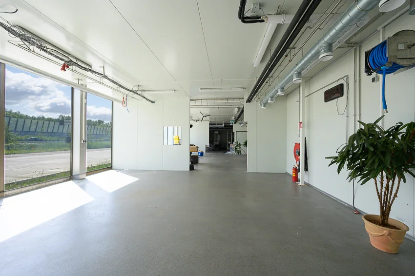 Lichte, industriële ruimte aan de Calandstraat met grote ramen, leidingen aan het plafond en enkele planten.