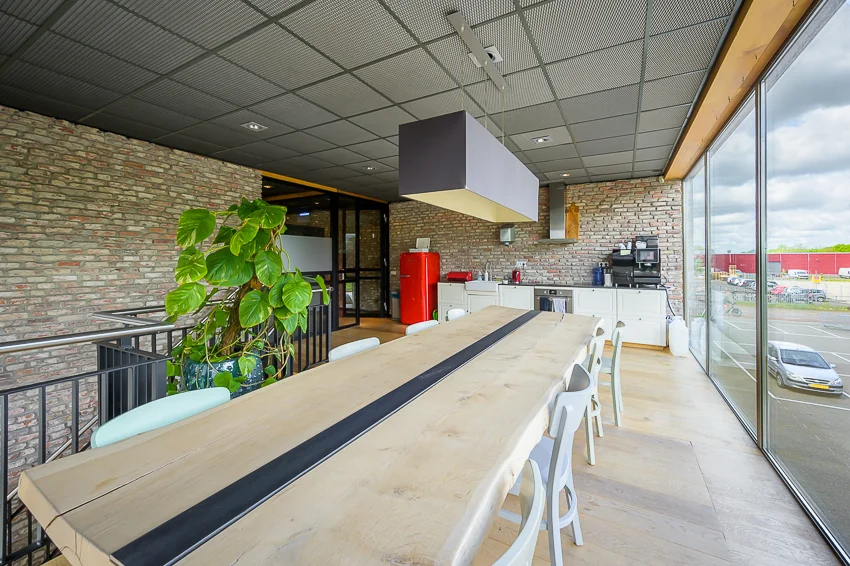 Moderne kantoorkeuken aan de Calandstraat met houten eettafel, bakstenen muren en uitzicht op de parkeergarage.