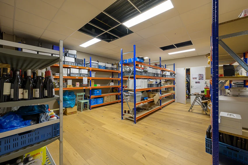 Opslagruimte aan de Calandstraat met stalen rekken gevuld met dozen, mappen en flessen.