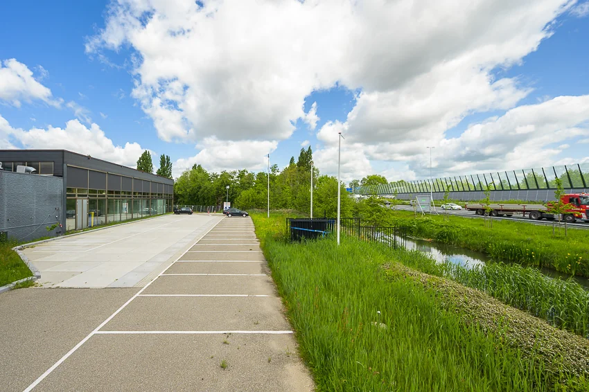 Leeg parkeerterrein aan de Calandstraat met naastgelegen groenstrook en snelweg op de achtergrond.