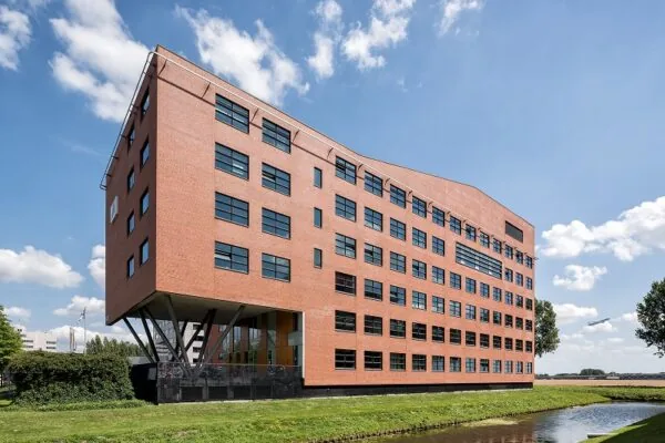 Modern rood bakstenen kantoorgebouw aan de Siriusdreef, met opvallende V-vormige steunpilaren en ligging aan een waterpartij.