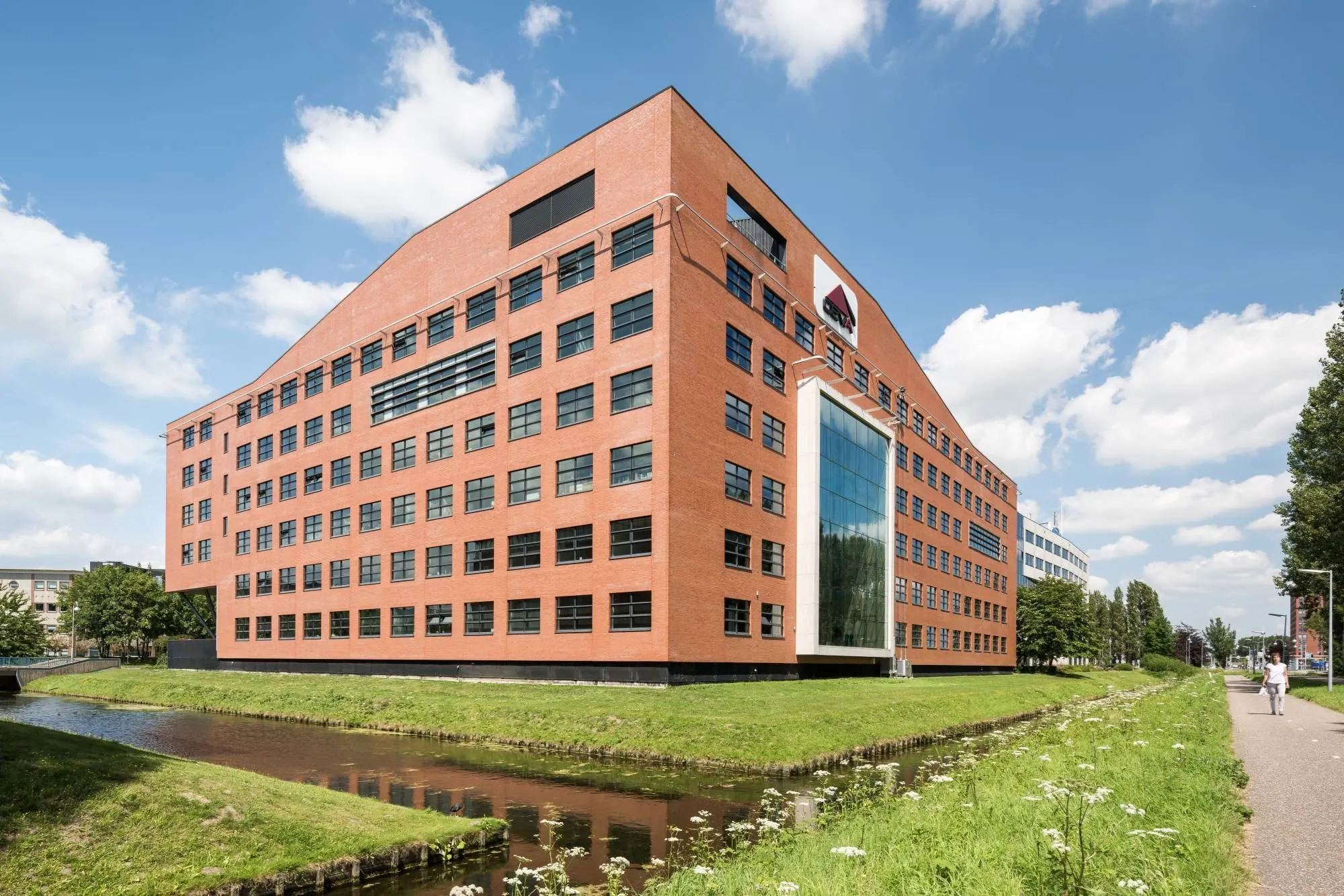 Modern rood bakstenen kantoorgebouw aan de Siriusdreef met grote glazen gevel en aangrenzend fietspad langs een waterloop.