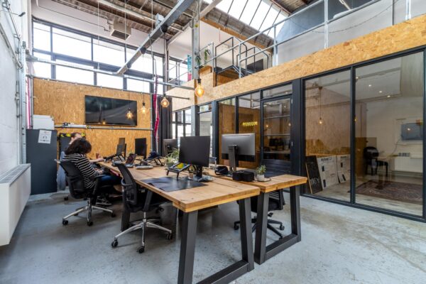 Modern industrieel kantoorinterieur aan de Eendrachtlaan met houten werkplekken, glazen vergaderruimte en zichtbare plafondconstructie.