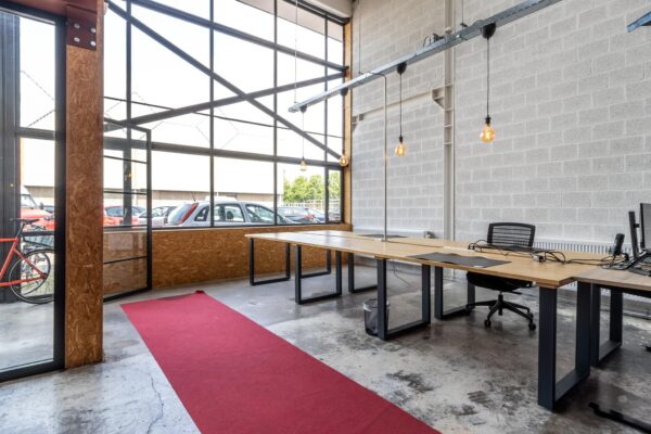 Industrieel ingerichte kantoorruimte aan de Eendrachtlaan met grote ramen, houten bureaus en een rode loper op betonnen vloer.