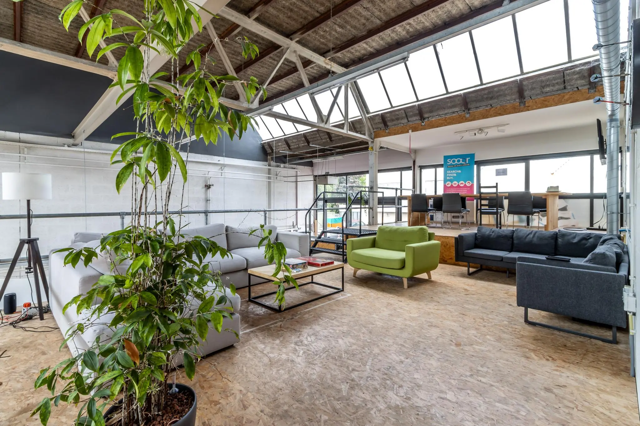 Open en licht industrieel kantoorinterieur aan de Eendrachtlaan met moderne zithoeken, planten en werkplekken op een verhoogd platform.