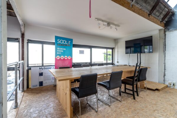 Vergaderruimte met houten tafel, zwarte stoelen, een televisiescherm en een Sooqr-banner in een industriële kantooromgeving op de Eendrachtlaan.