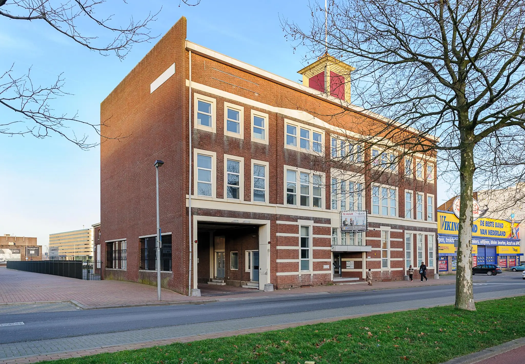 Voormalig schoolgebouw aan de Stadionweg in Rotterdam met een karakteristieke rode bakstenen gevel en te huur-bord aan de voorzijde.