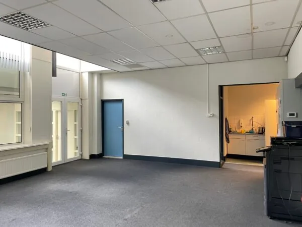 Kantoorruimte aan de Stadionweg met grijze vloerbedekking, een open pantry en meerdere deuren naar aangrenzende ruimtes.