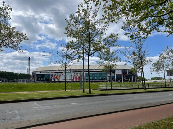 Uitzicht op Stadion Feijenoord (De Kuip) vanaf de Stadionweg met bomen en weg op de voorgrond.