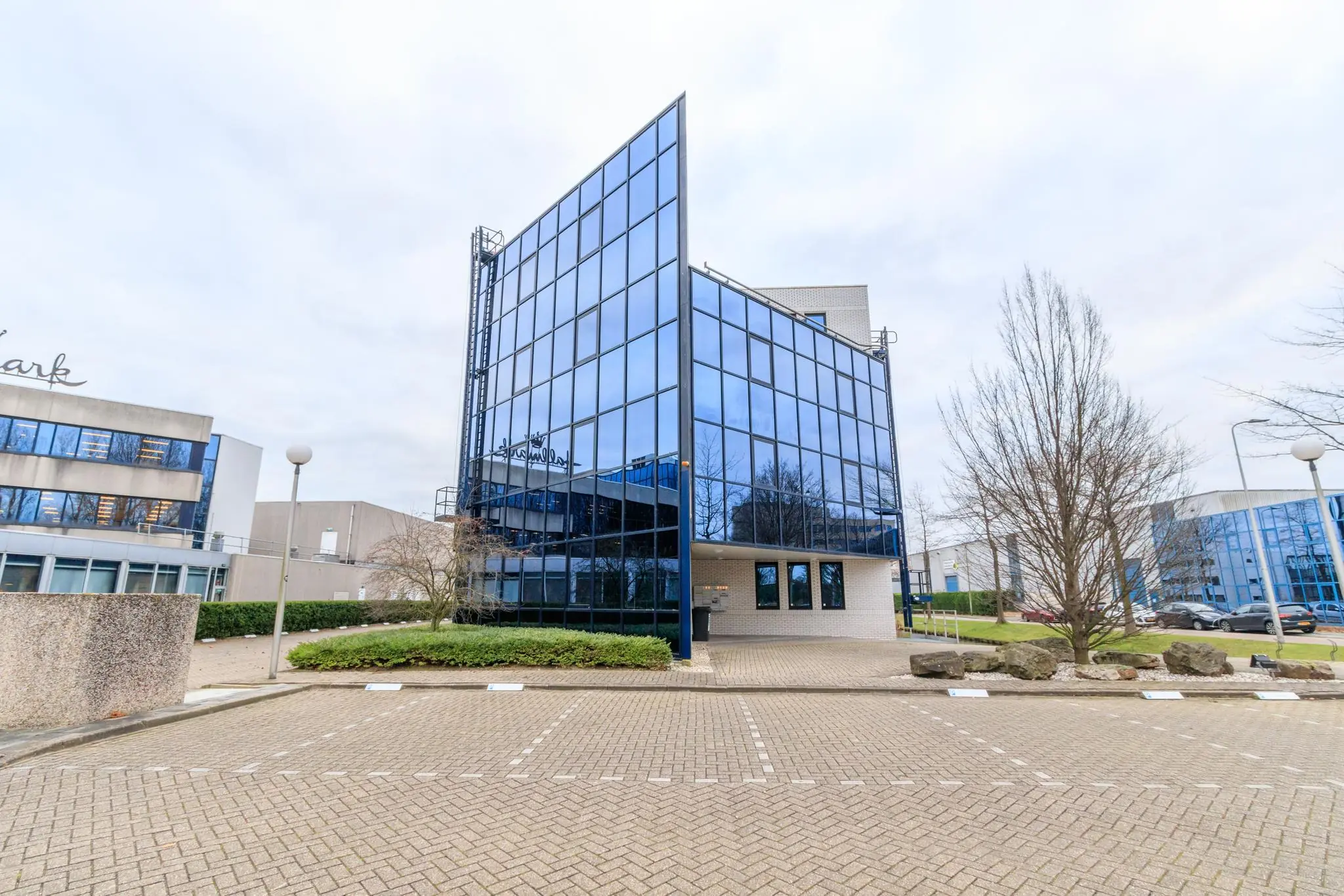 Kantoorgebouw met spiegelende glasgevel aan de Vlierbaan, met lege parkeerplaatsen op de voorgrond.