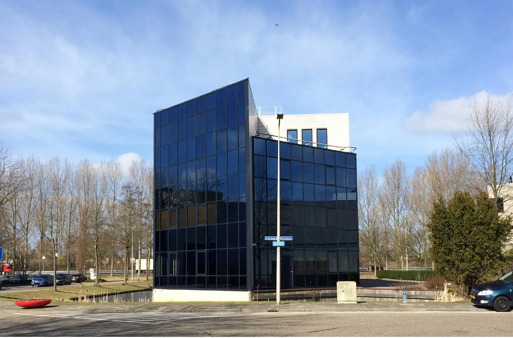 Een modern kantoorgebouw met spiegelende gevel aan de Vlierbaan, gelegen aan een rustige straat met bomen op de achtergrond.