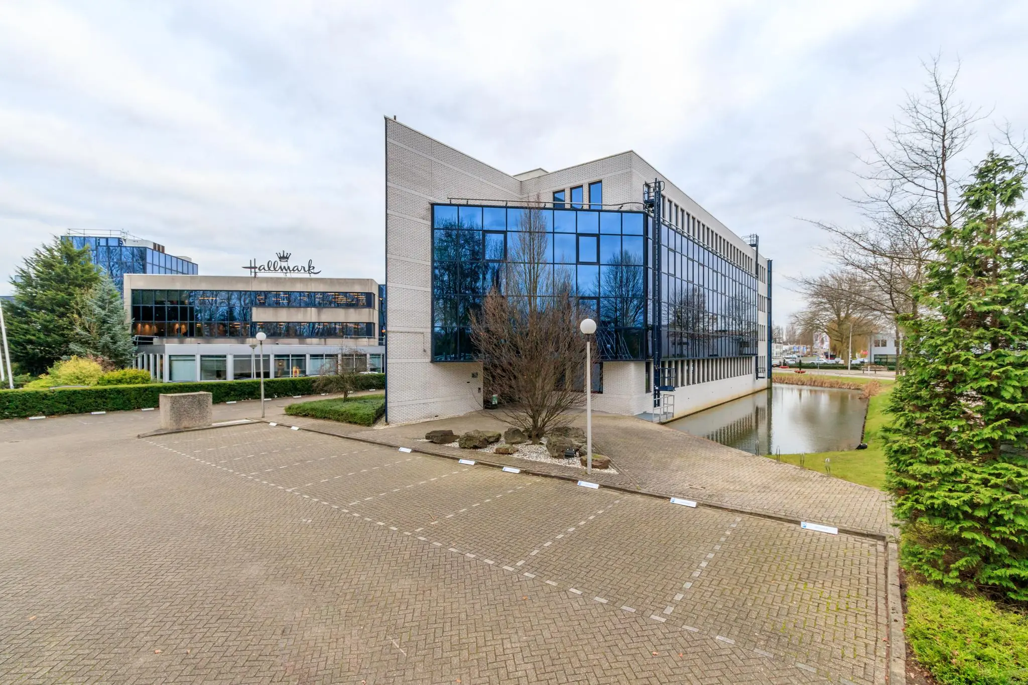Modern kantoorpand aan de Vlierbaan met Hallmark-gebouw op de achtergrond en een parkeervoorziening op de voorgrond.