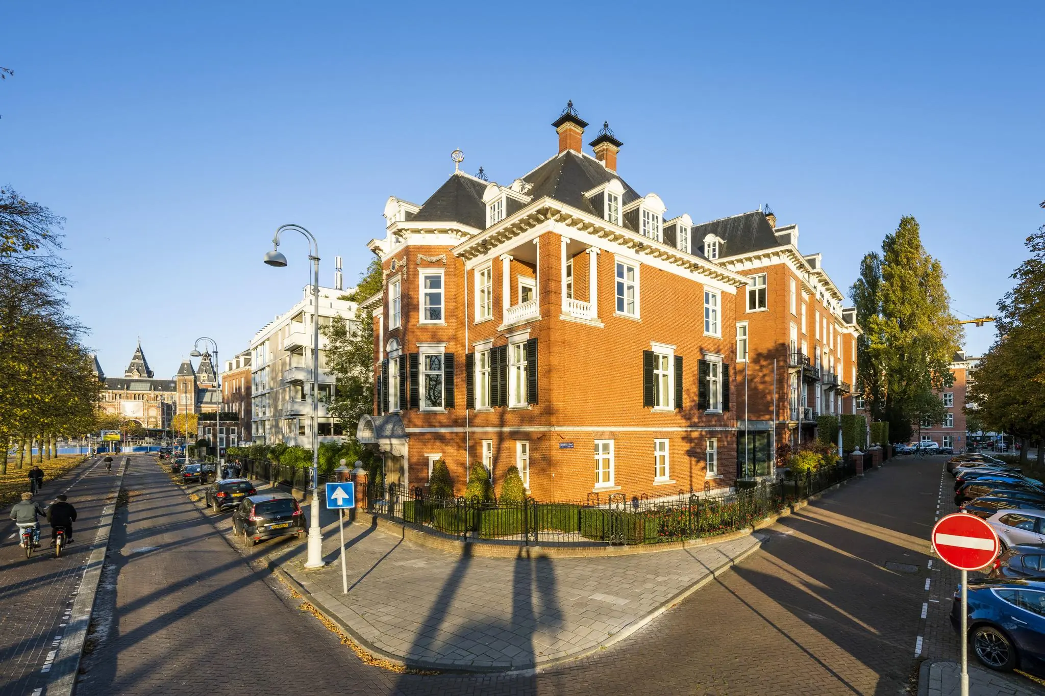 Hoekpand met rode bakstenen aan het Museumplein in Amsterdam, met op de achtergrond het Rijksmuseum.