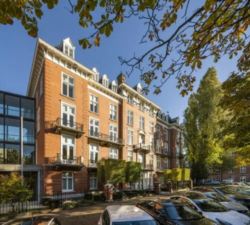 Monumentaal herenhuis aan het Museumplein in Amsterdam, omringd door bomen en geparkeerde auto's.
