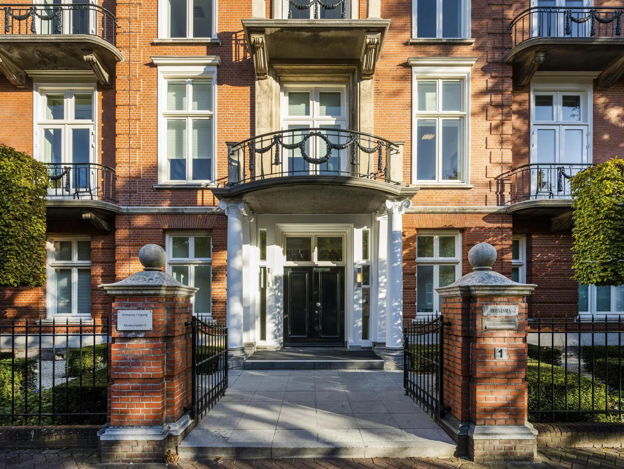 Ingang van een klassiek herenhuis aan het Museumplein in Amsterdam met symmetrische gevel en smeedijzeren hek.