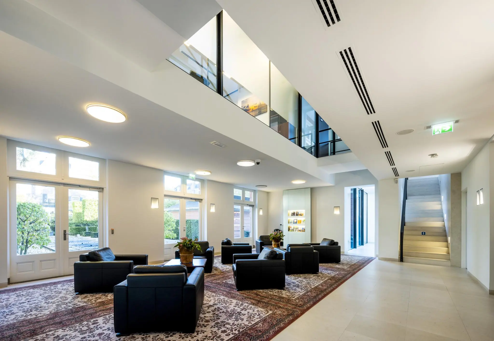 Moderne en lichte lounge in een gebouw aan het Museumplein met zwarte zitplaatsen, Perzische tapijten en een open trap naar de bovenverdieping.