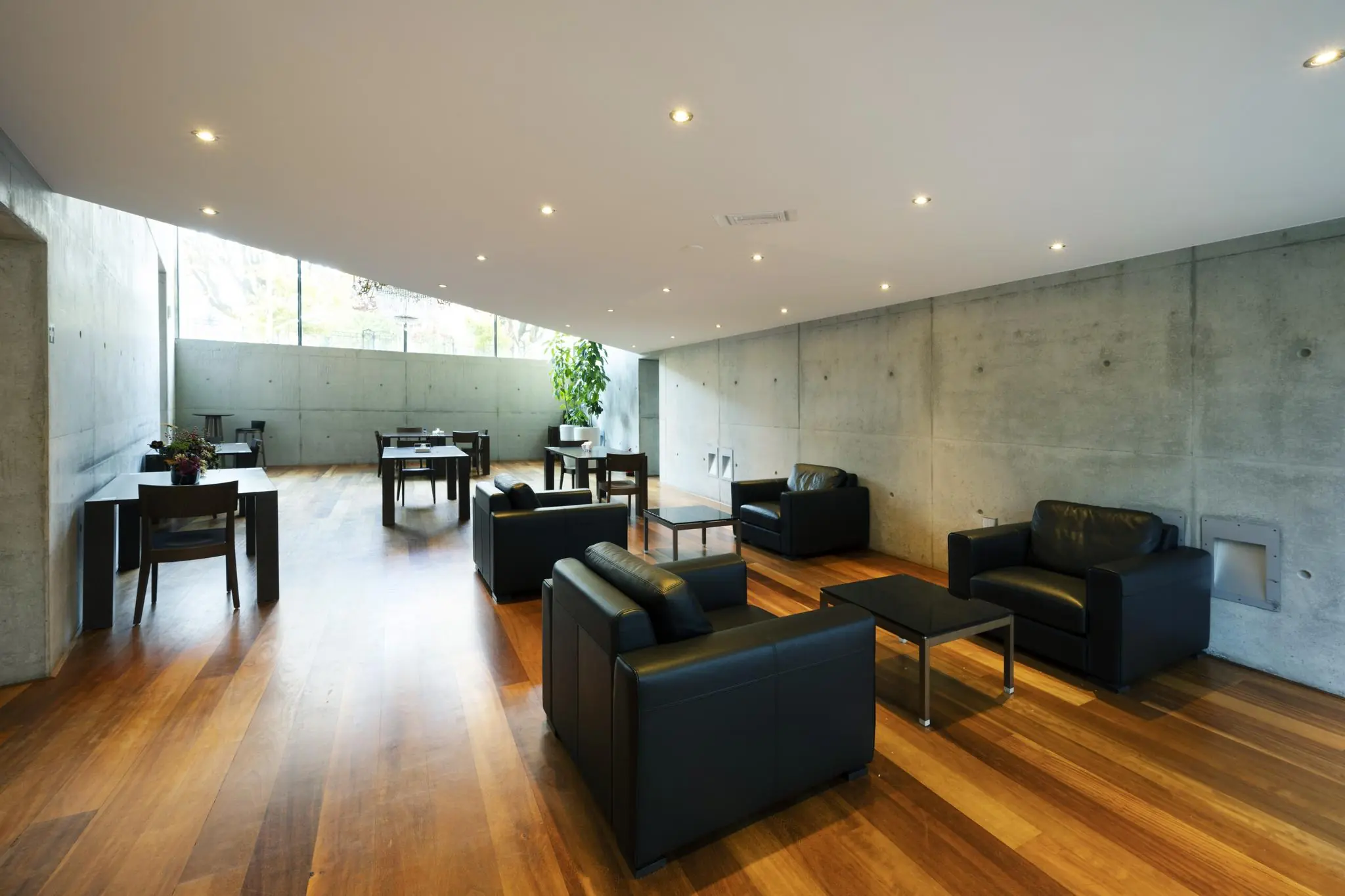 Moderne lounge op het Museumplein met zwart lederen fauteuils, houten vloer en betonnen wanden.