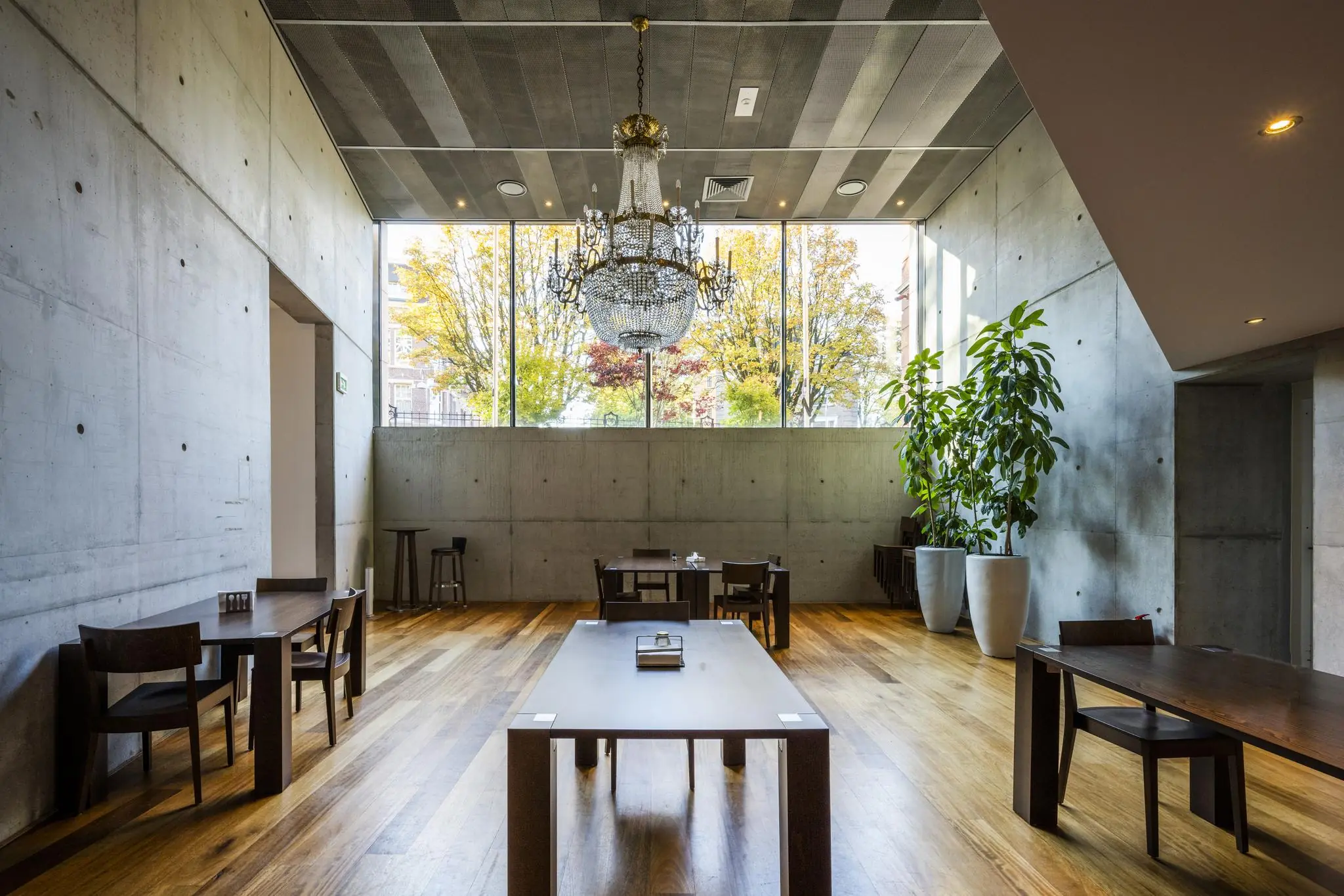 Moderne, minimalistisch ingerichte ruimte in het Museumplein met betonnen muren, houten vloeren, grote ramen en een kristallen kroonluchter.