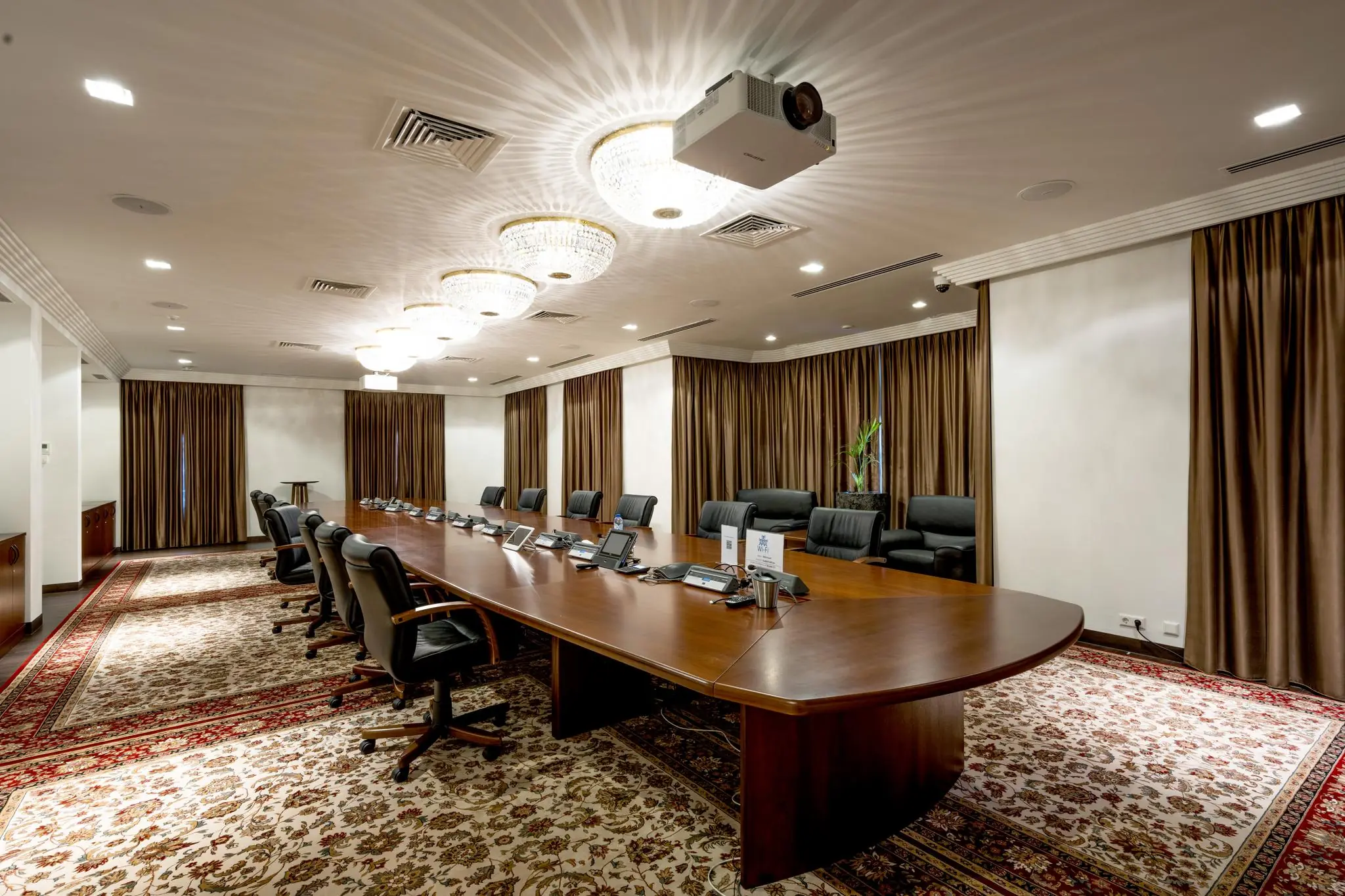 Luxe vergaderruimte met een lange houten tafel, lederen stoelen, plafondverlichting en een projector aan het plafond.