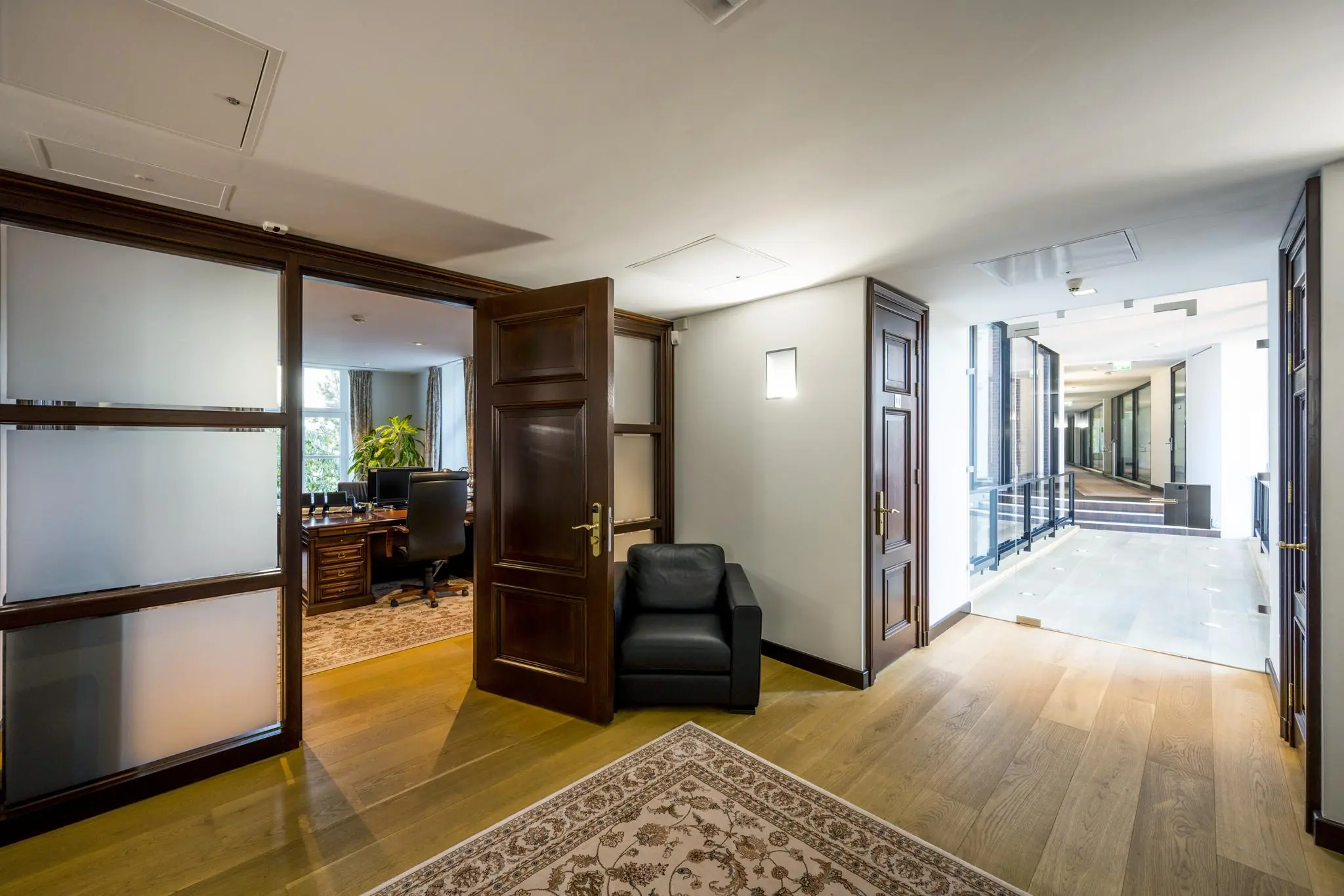 Luxe kantoorgang op het Museumplein met open deur naar klassiek ingericht kantoor met houten meubels.