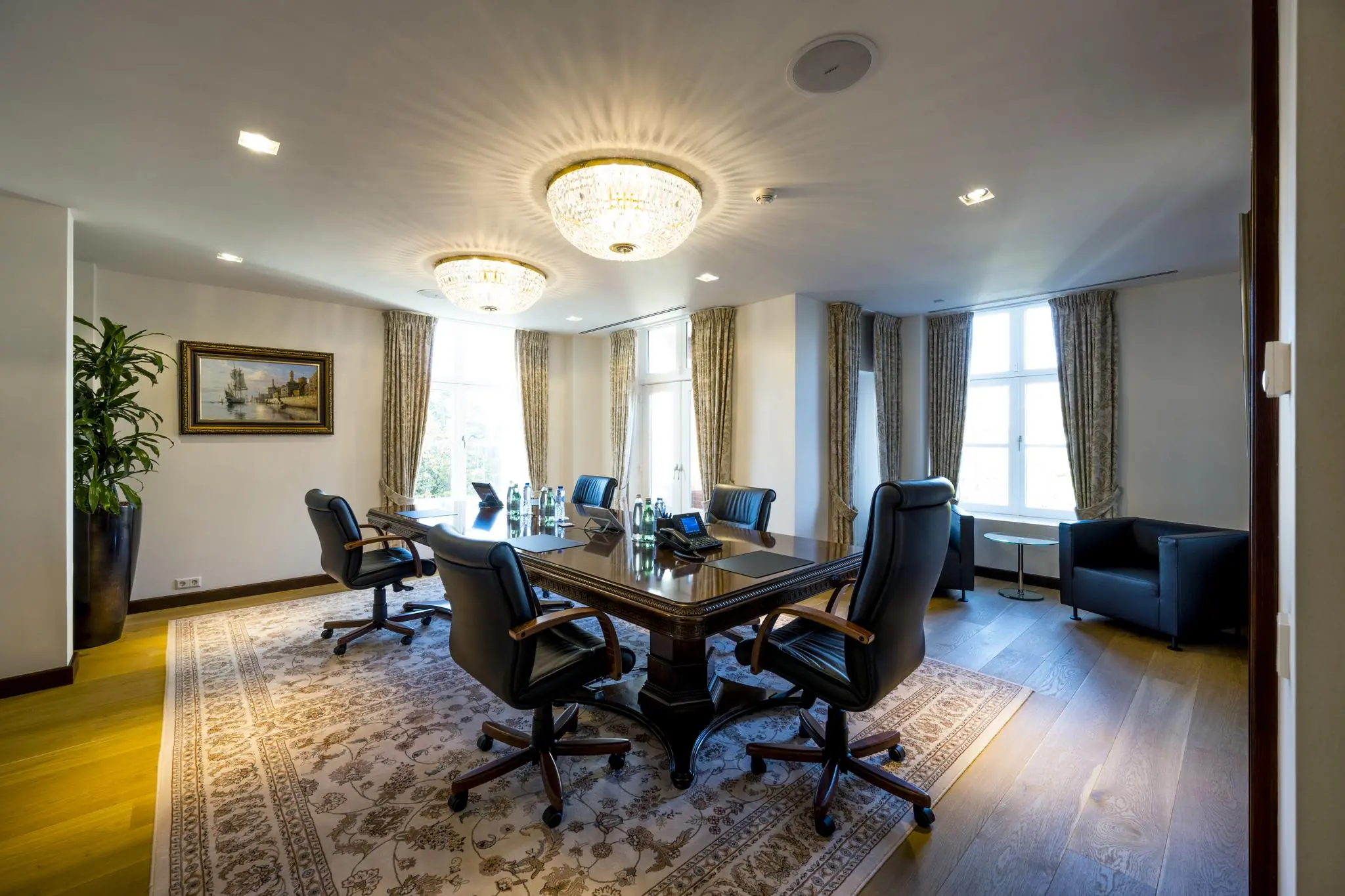 Luxe vergaderruimte op het Museumplein met een houten tafel, lederen stoelen, grote ramen en kristallen plafondlampen.