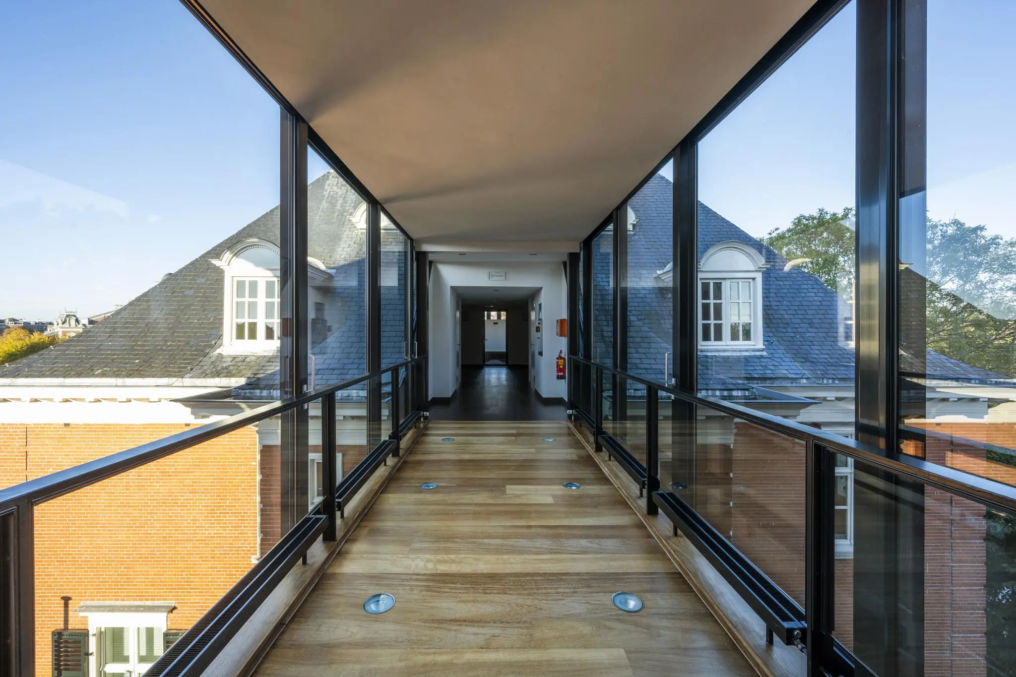 Glazen loopbrug met houten vloer tussen gebouwen op het Museumplein in Amsterdam.
