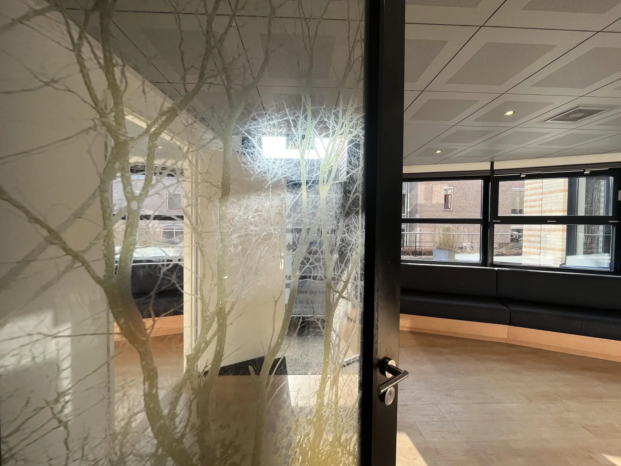 Glazen deur met boommotief die toegang geeft tot een moderne wachtruimte aan de Amersfoortseweg.