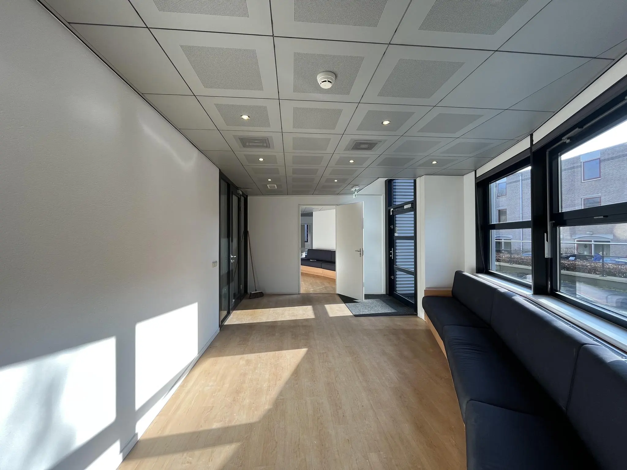 Moderne wachtruimte aan de Amersfoortseweg met houten vloer, zwarte zitbanken en grote raampartijen.