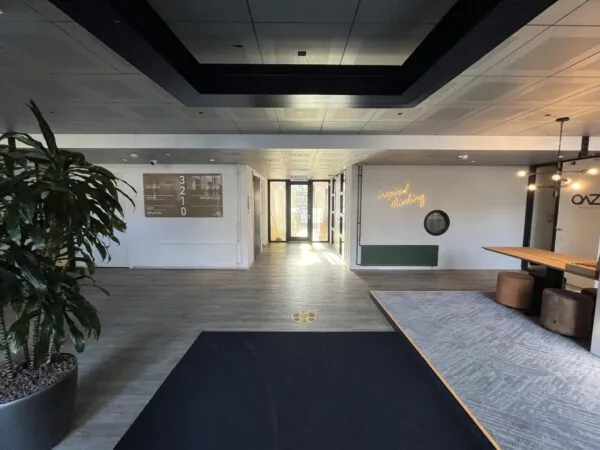 Moderne entreehal aan de Amersfoortseweg met houten vloer, neontekst "inspired thinking" en een vergadertafel rechts.
