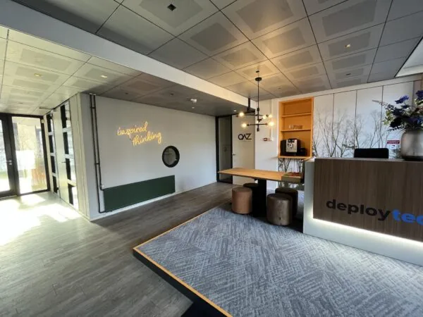 Moderne kantoorentree aan de Amersfoortseweg met balie van Deployteq, zitgedeelte en neontekst "inspired thinking" op de muur.