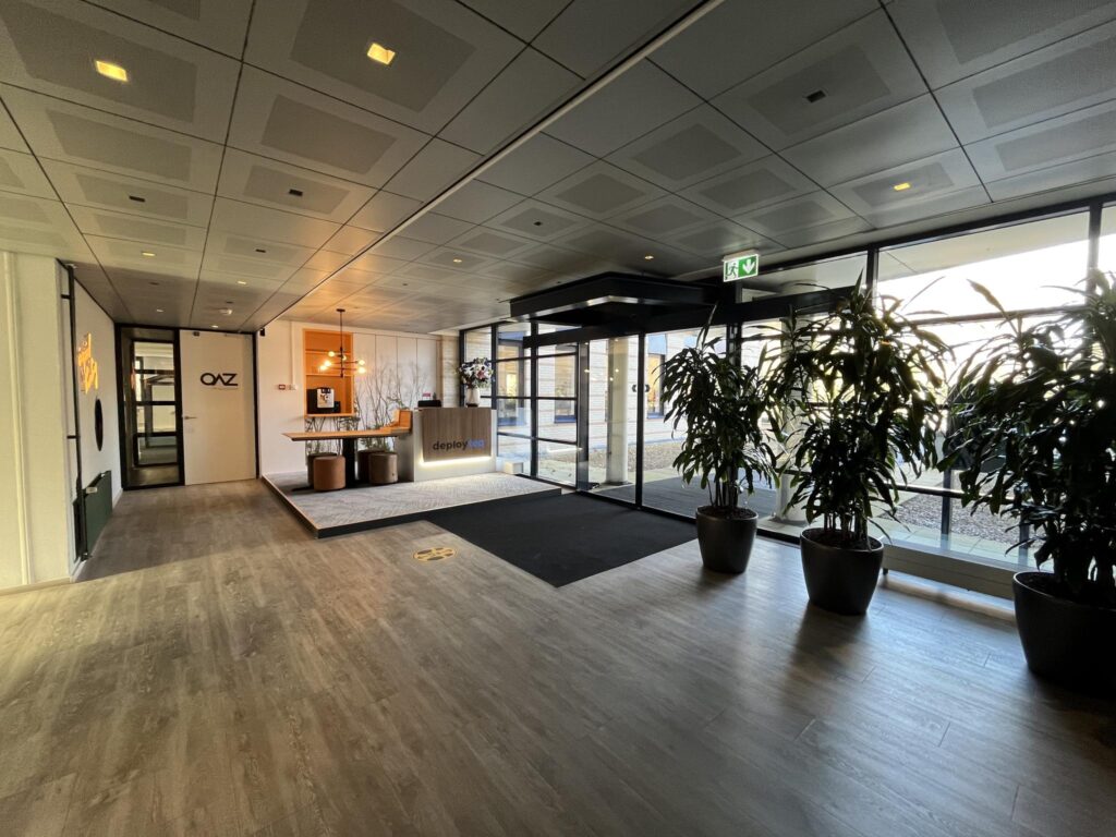 Moderne entreehal met receptiebalie van Deployteq aan de Amersfoortseweg, ingericht met grote planten en glazen schuifdeuren.