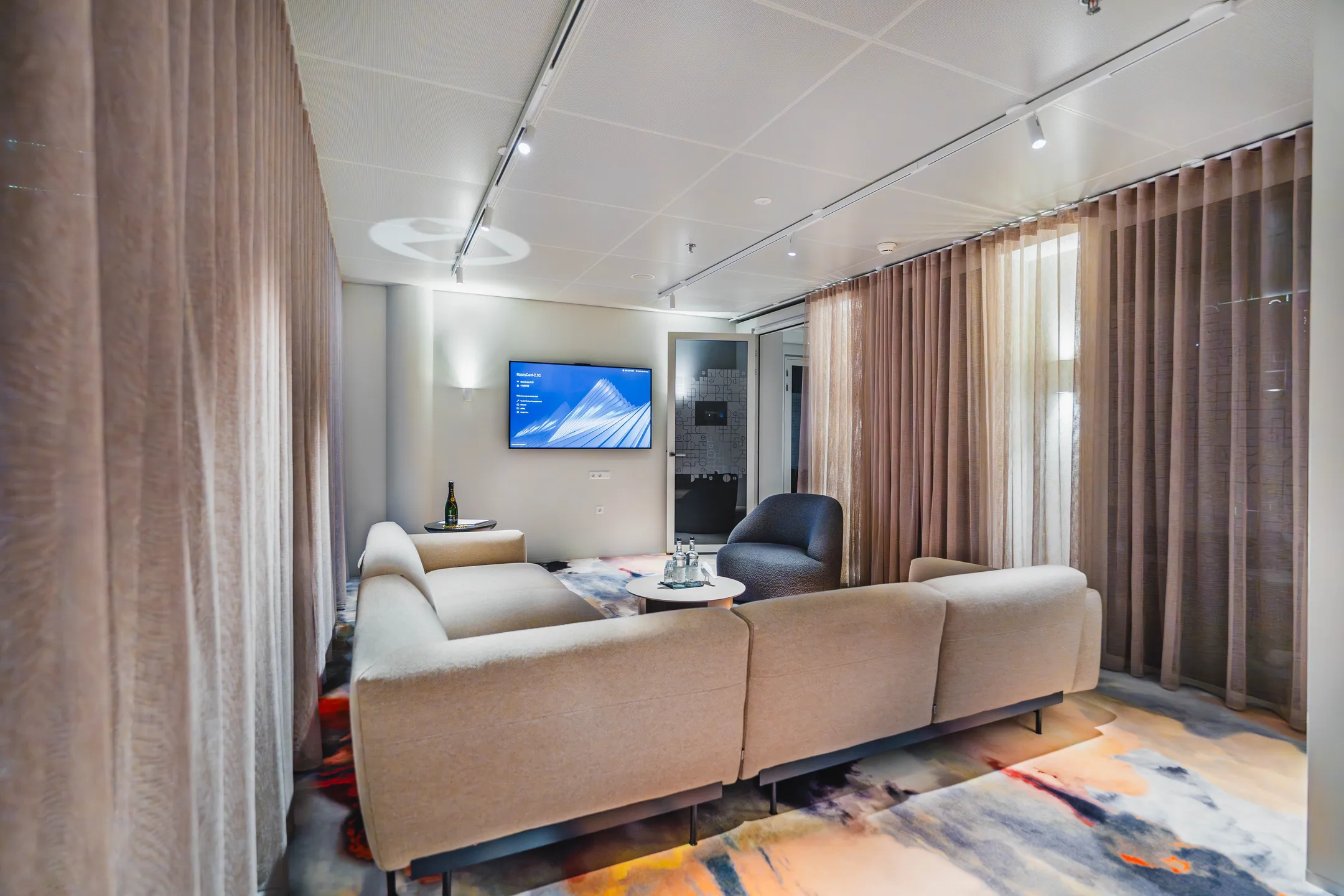 Een moderne zithoek met beige banken en een flatscreen-tv aan de muur.