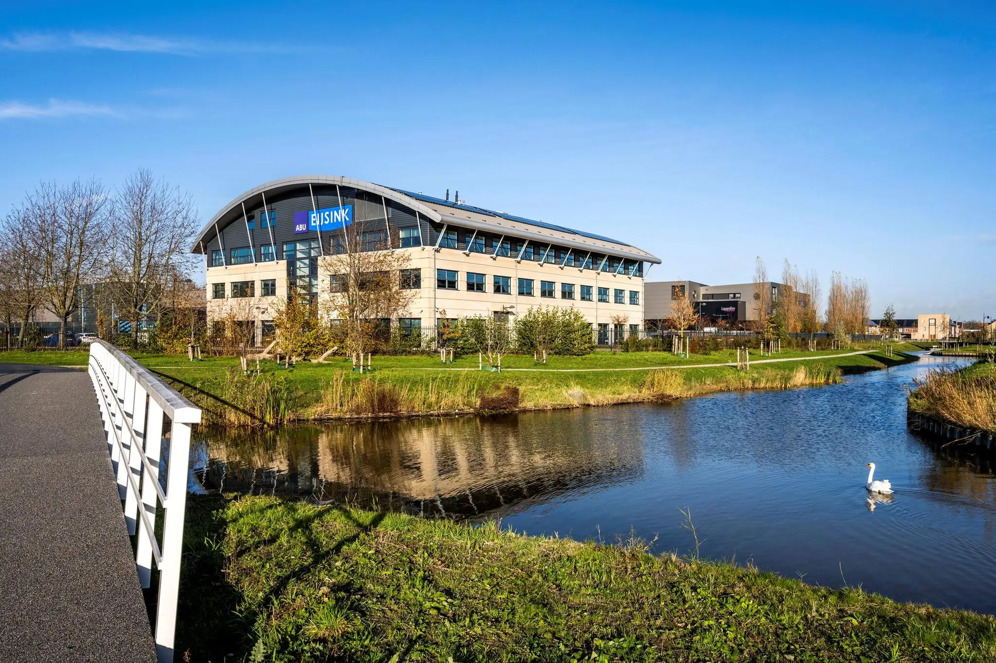 Kantoorpand van Eijsink aan de Singaporestraat, gelegen aan het water met een witte brug en een zwaan op de voorgrond.