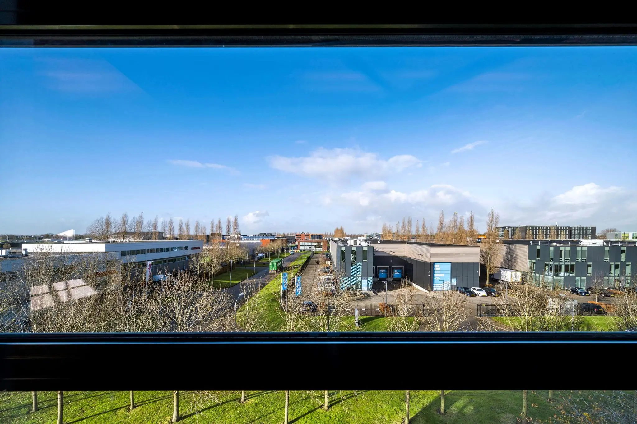 Uitzicht op bedrijventerrein aan de Singaporestraat met moderne bedrijfspanden, wegen en bomen onder een blauwe lucht.