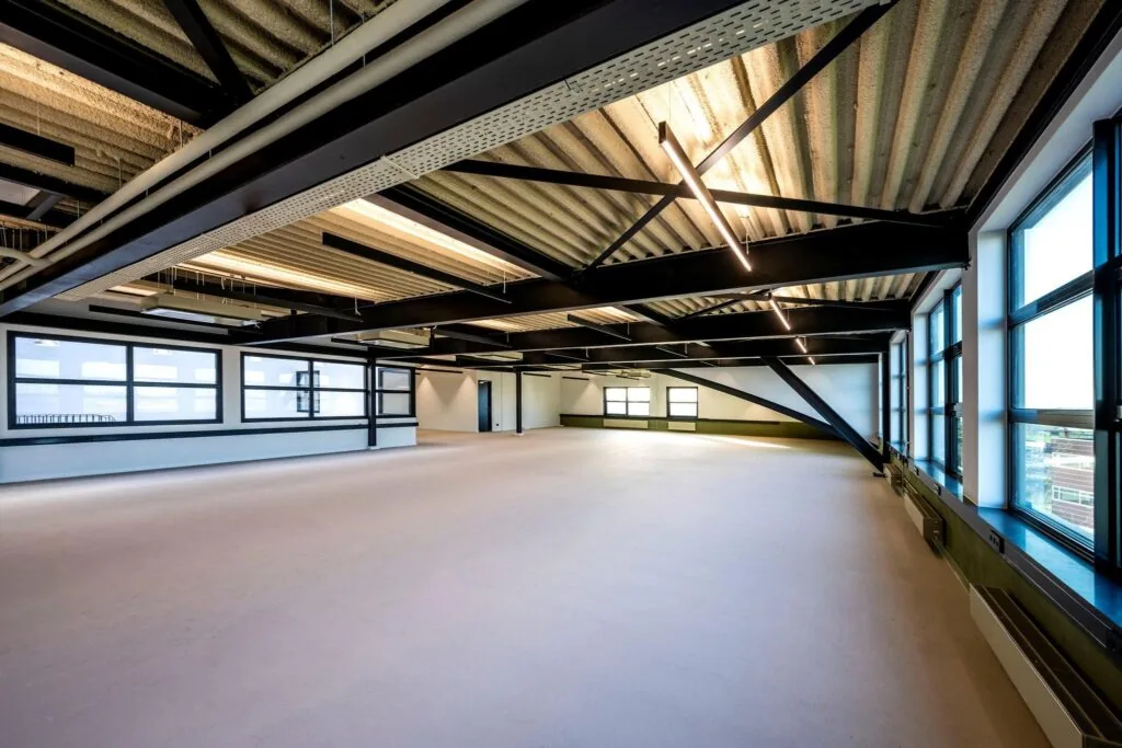 Licht en ruim industrieel kantoorinterieur aan de Singaporestraat met grote ramen en zichtbare plafondconstructie.