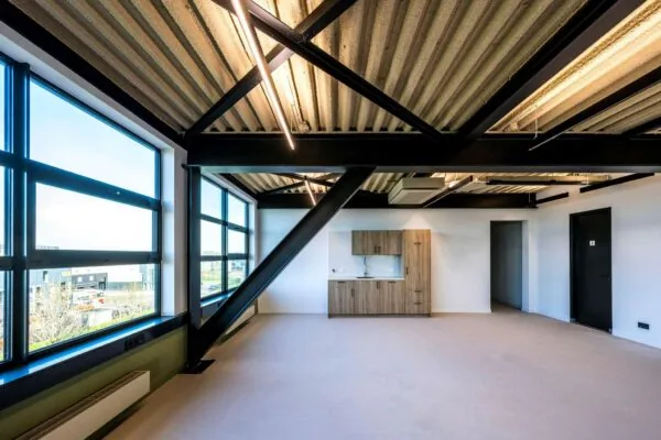 Modern, licht kantoorinterieur aan de Singaporestraat met grote ramen, zichtbare plafondconstructie en ingebouwde kitchenette.