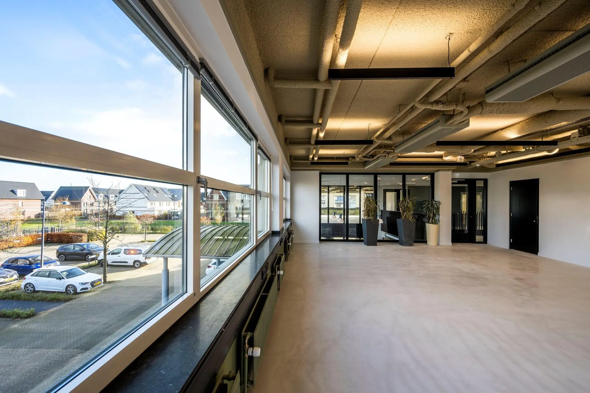 Licht en ruim kantoorpand aan de Singaporestraat met grote ramen en zicht op geparkeerde auto's en woonhuizen.