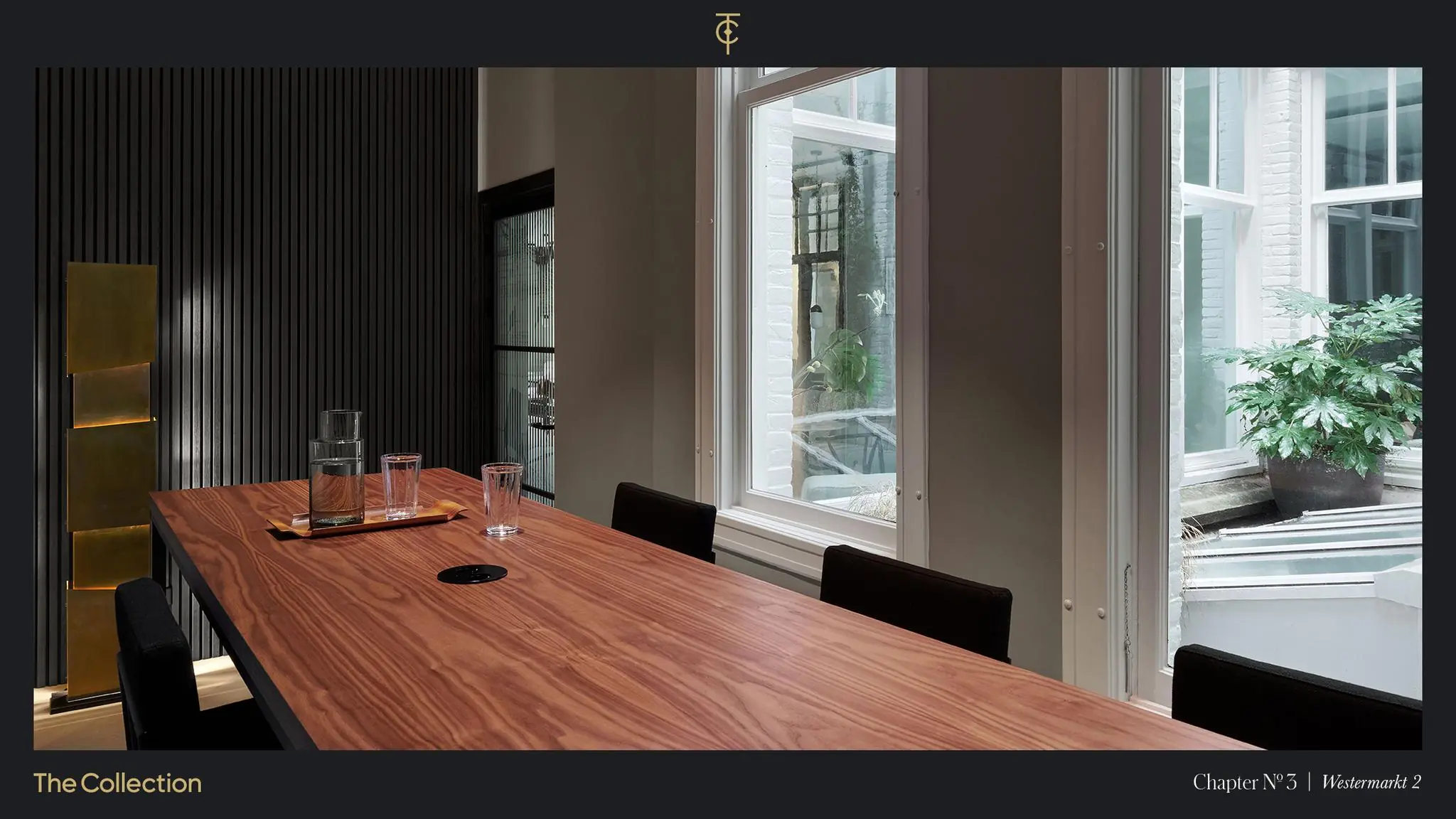 Strak vormgegeven vergaderruimte aan de Westermarkt met houten tafel, glazen karaffen en uitzicht op een binnentuin met grote plant.